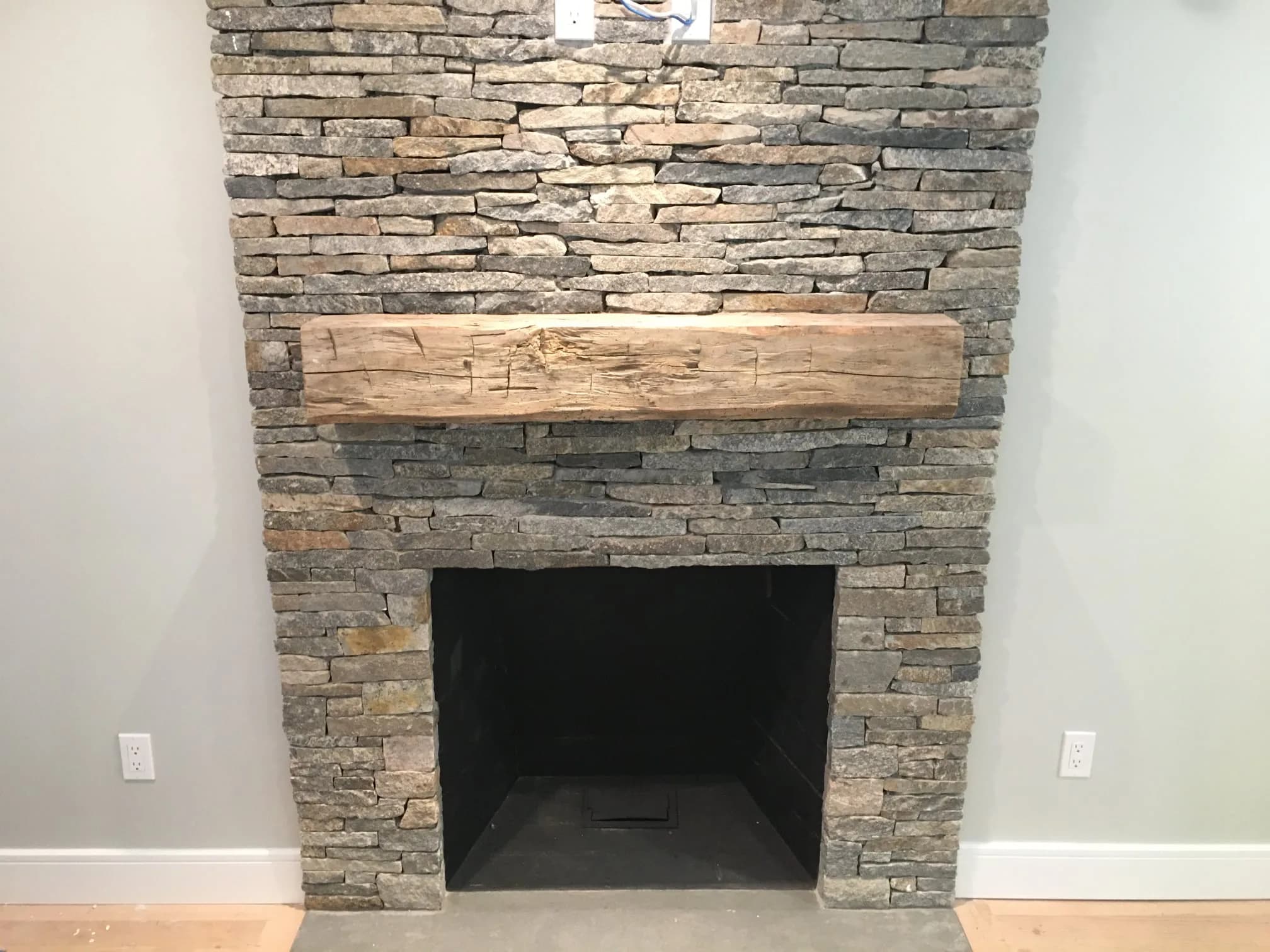 Hand-hewn reclaimed mantel centered on a stacked stone fireplace